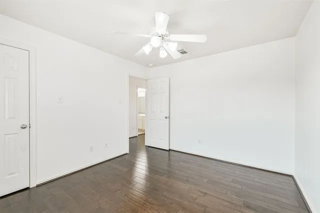 an empty room with wooden floor fan and windows