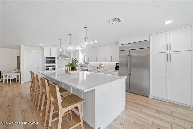 a large white kitchen with kitchen island a stove a refrigerator a dining table and chairs with wooden floor