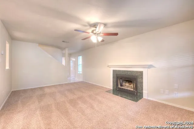 a view of an empty room with chandelier fan and fire place