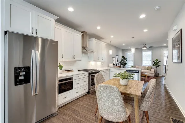 a kitchen with stainless steel appliances granite countertop a refrigerator a stove a sink a dining table and chairs with wooden floor