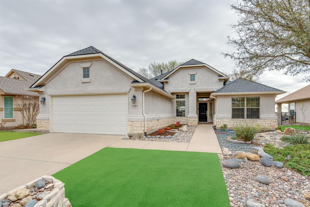 Traditional-style house with stucco siding, stone siding, driveway, and a shingled roof