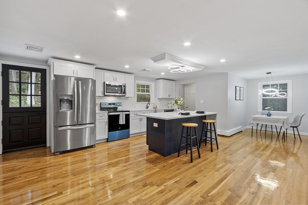 a kitchen with stainless steel appliances granite countertop a refrigerator a stove top oven and a dining table with wooden floor