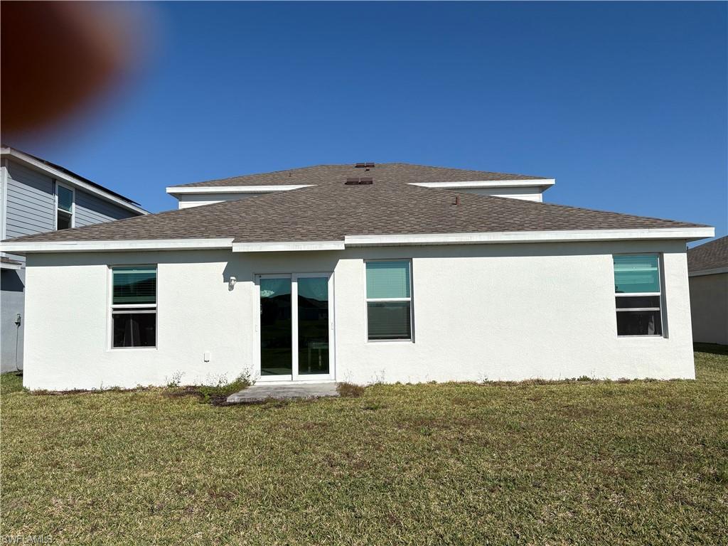 19891 Green Pasture Road Lehigh Acres, FL 33936 - Photo 4 of 5 Rear view of house with roof with shingles, a lawn, and stucco siding