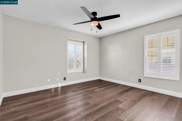 an empty room with wooden floor fan and windows