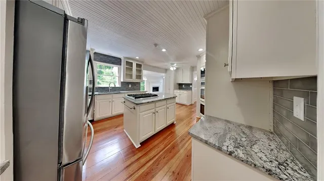 a large kitchen with a refrigerator a sink dishwasher a stove and white cabinets with wooden floor