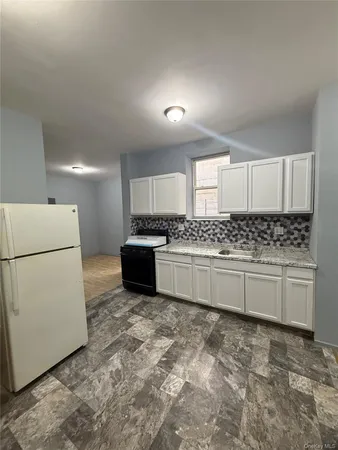 a kitchen with granite countertop a refrigerator sink stove and white cabinets