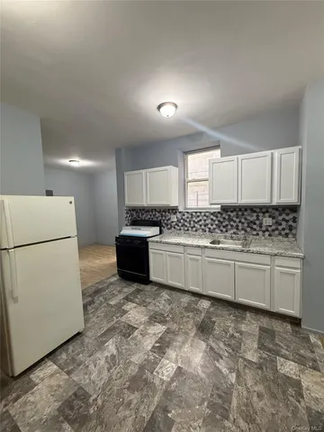 a kitchen with granite countertop a refrigerator sink stove and white cabinets