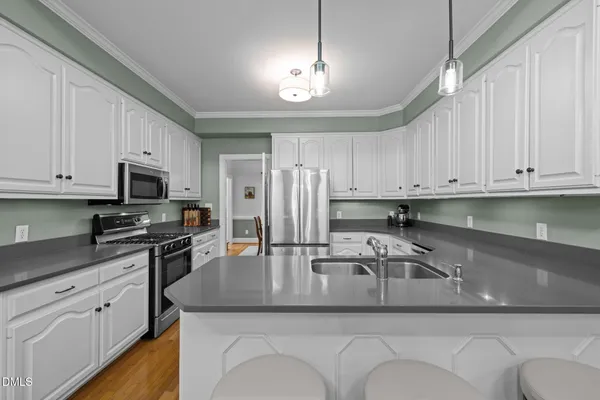 a kitchen with stainless steel appliances granite countertop a refrigerator a sink a stove a dining table and chairs with wooden floor