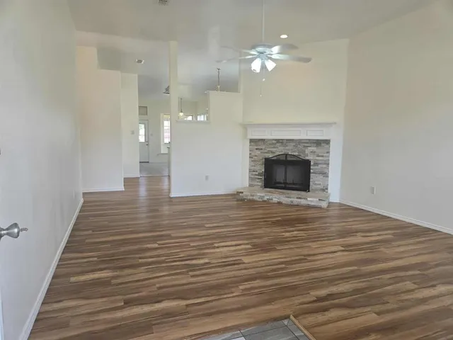 a view of an empty room with wooden floor and a fireplace
