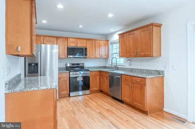 a kitchen with stainless steel appliances granite countertop a refrigerator a sink dishwasher a stove with wooden cabinets and floor