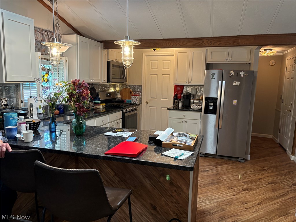 8701 Mayfield Road, Unit 148 Chesterland, OH 44026 - Photo 4 of 24 Spacious kitchen featuring an island with a dark countertop and wood-finish paneling, overhead pendant lighting, stainless steel appliances, white cabinetry, and wood-finish flooring