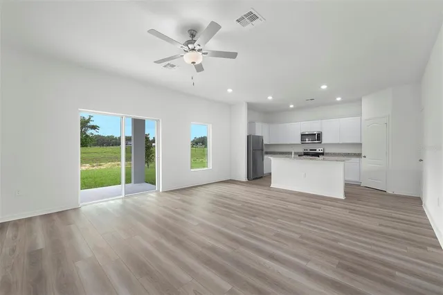 a view of an empty room with kitchen and window