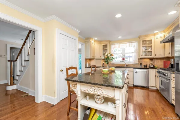 a kitchen with stainless steel appliances granite countertop a stove top oven a refrigerator a sink and white cabinets with wooden floor