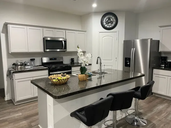 a kitchen with stainless steel appliances granite countertop a sink a stove a microwave a refrigerator a stove and white cabinets