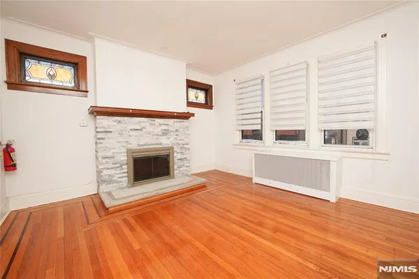 a view of an empty room with wooden floor fireplace and a window