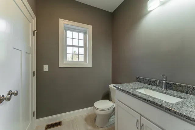 a bathroom with a granite countertop toilet a sink and a window