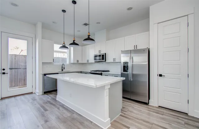 a kitchen with stainless steel appliances granite countertop a sink a stove a refrigerator and a island with wooden floor