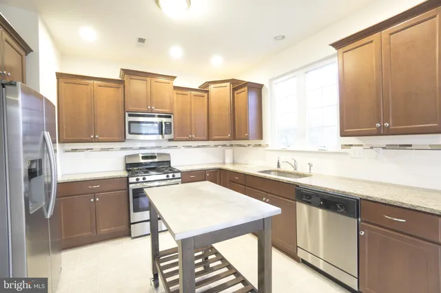 a kitchen with stainless steel appliances a sink a stove a refrigerator cabinets and a window
