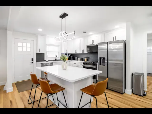 a kitchen with stainless steel appliances kitchen island granite countertop a dining table chairs and a refrigerator