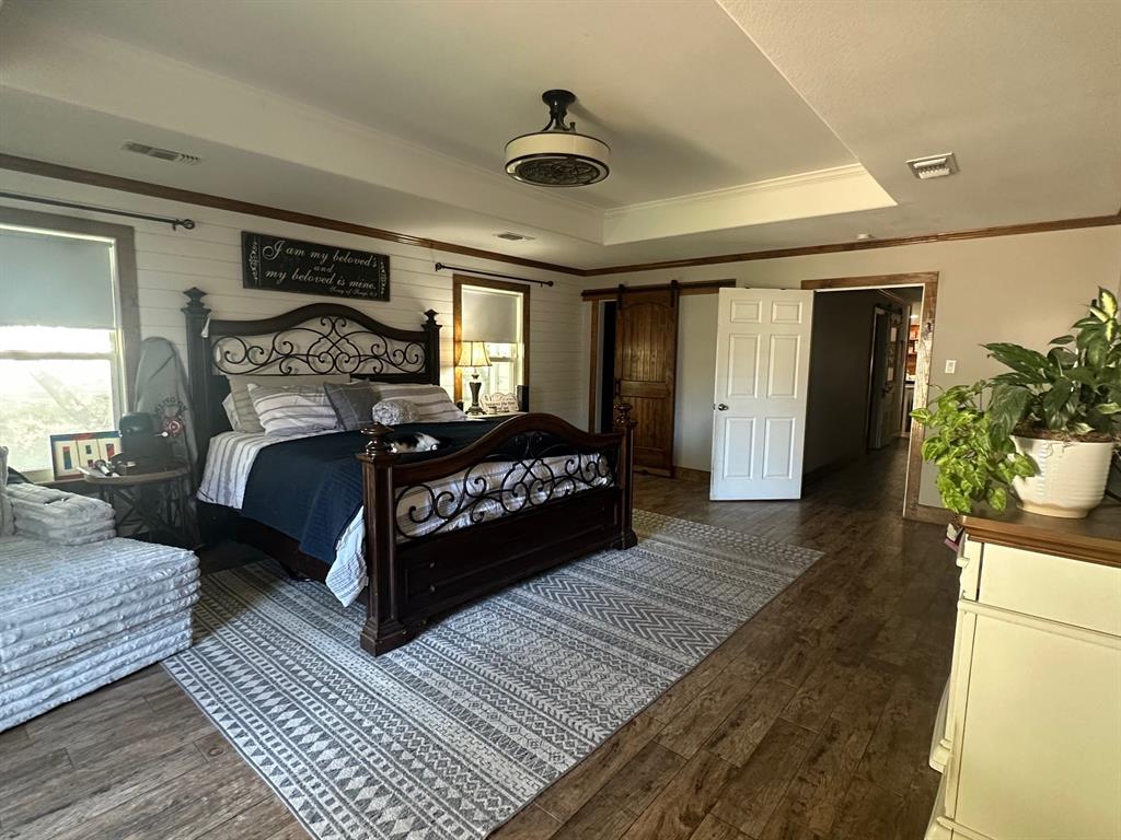 101 Twin Creek Road Comanche, TX 76442 - Photo 19 of 28 Bedroom with a barn door, a tray ceiling, dark wood-style floors, crown molding, and wooden walls