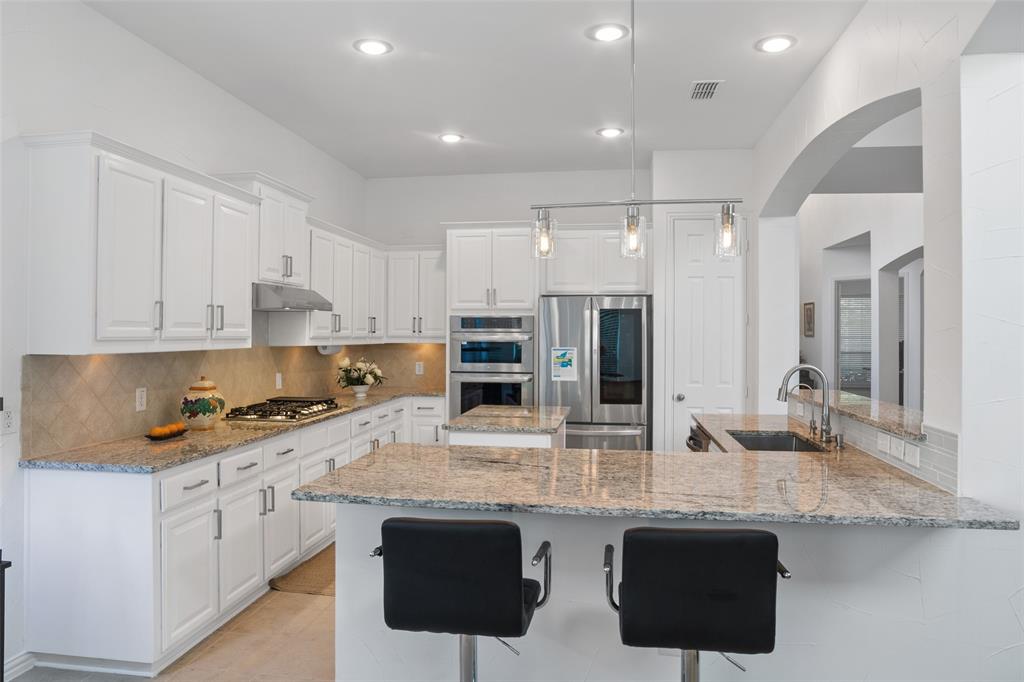 1818 Port Isabel Drive Allen, TX 75013 - Photo 7 of 38 a kitchen with stainless steel appliances granite countertop a stove top oven a sink a dining table and chairs with white cabinets
