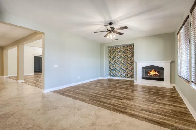 a view of a livingroom with a fireplace a ceiling fan and wooden floor