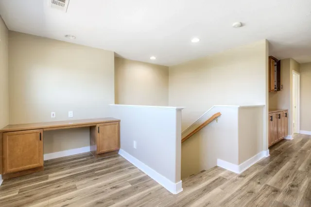 a view of an empty room with wooden floor and a kitchen
