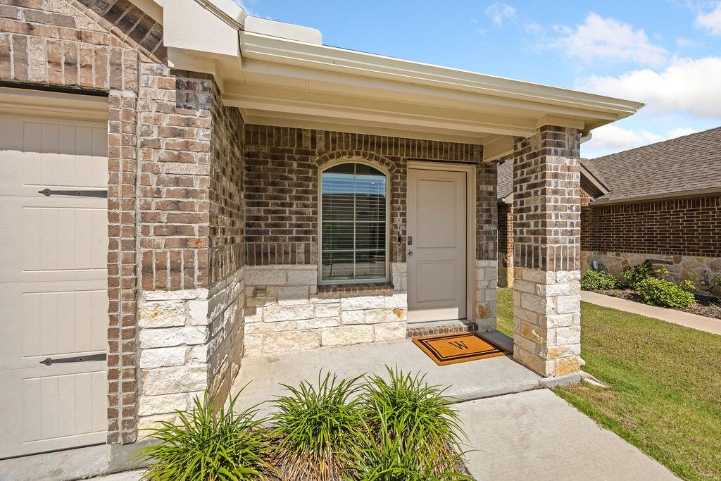 822 Ramble Road Lavon, TX 75166 - Photo 4 of 35 Welcoming covered entry featuring brick and stone veneer, an arched window, a paneled front door, and a concrete walkway