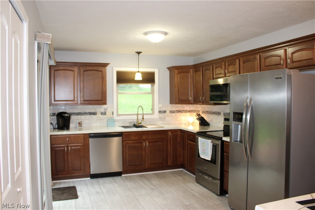 202 Home Street Rittman, OH 44270 - Photo 24 of 47 Kitchen featuring wood-finish cabinetry, stainless steel appliances, a tile backsplash, light-toned countertops, and wood-look flooring