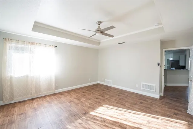 an empty room with wooden floor ceiling fan and windows