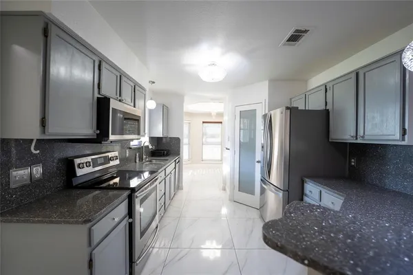 a kitchen with stainless steel appliances granite countertop a refrigerator a stove and a sink with wooden cabinets