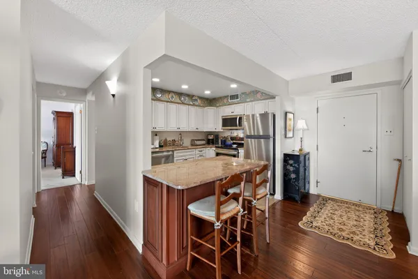 a kitchen with stainless steel appliances kitchen island granite countertop a refrigerator a stove a sink a dining table and chairs with wooden floor
