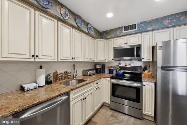 a kitchen with stainless steel appliances granite countertop a refrigerator a stove a sink and white cabinets