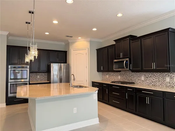 a large kitchen with stainless steel appliances kitchen island granite countertop a refrigerator a stove and a sink with wooden cabinets