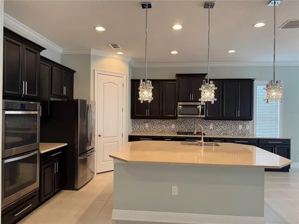 a large kitchen with kitchen island a large counter top stainless steel appliances and cabinets