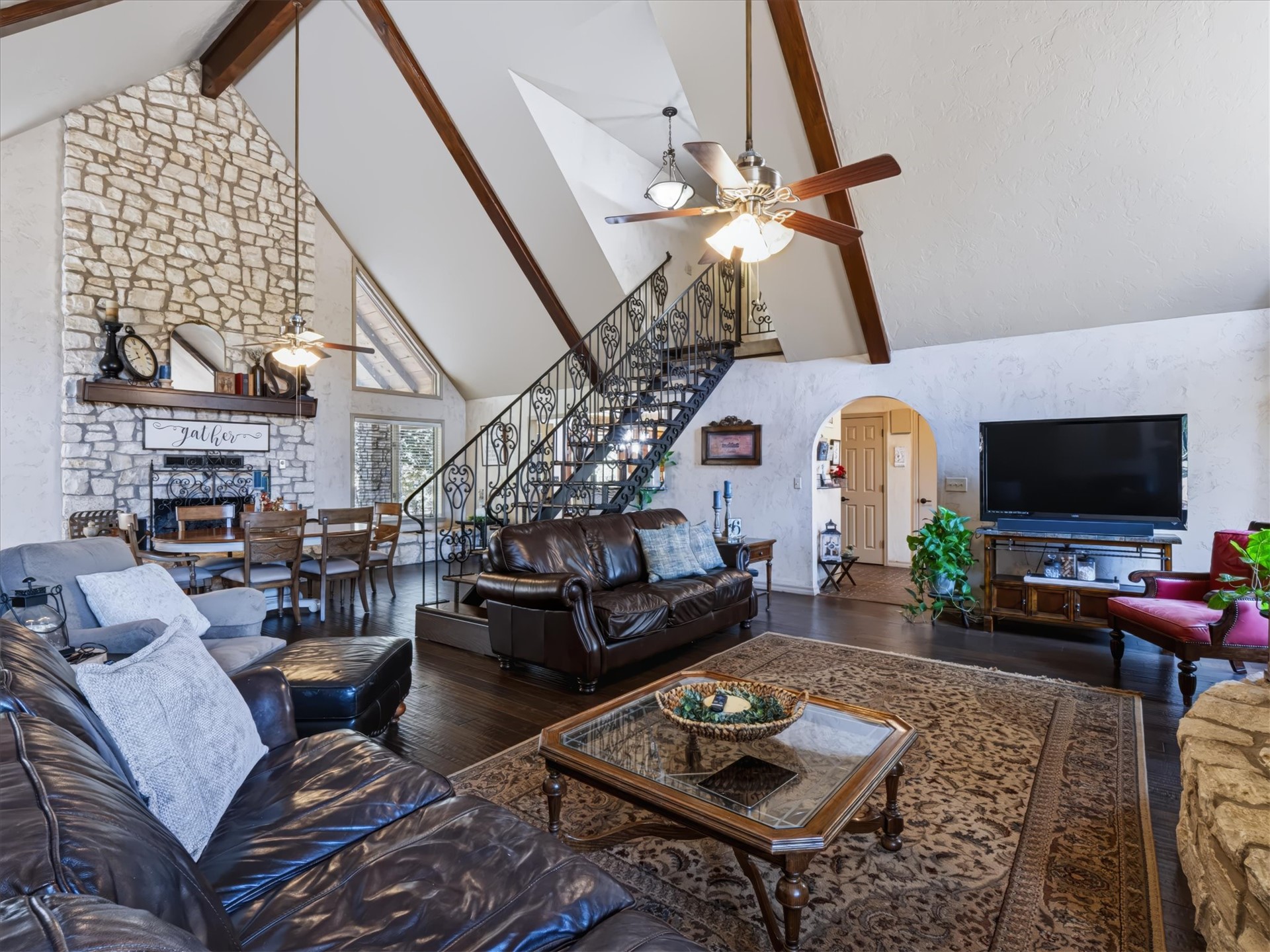 1133 West Chicken Fight Road Atoka, OK 74525 - Photo 10 of 49 Vaulted ceilings with exposed wood beams, a floor-to-ceiling stone fireplace, dark wood-finish flooring, and a wrought iron staircase with decorative balusters