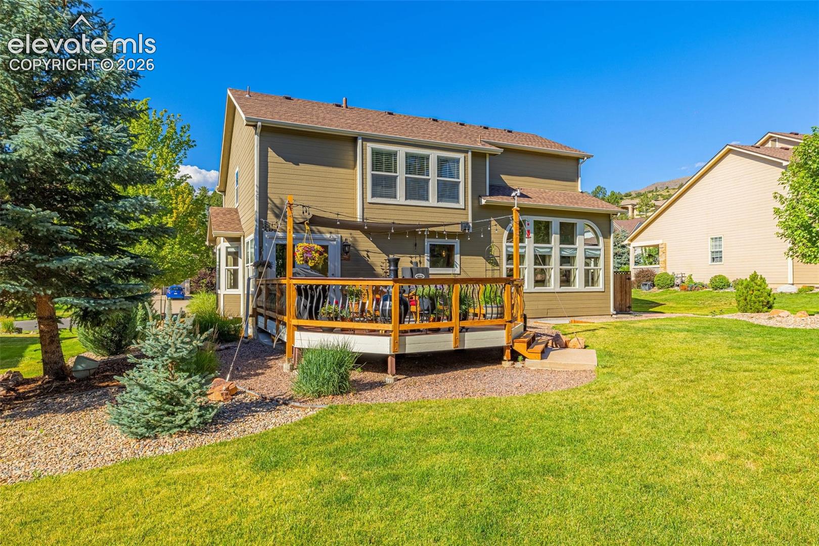 7985 Orchard Path Road Colorado Springs, CO 80919 - Photo 47 of 50 Expansive backyard featuring a manicured lawn, established landscaping, and a multi-level deck with wooden railings