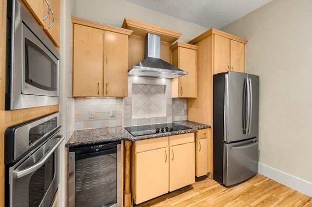 a kitchen with stainless steel appliances granite countertop a refrigerator a stove and a sink with wooden floor