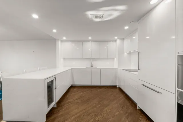 a large white kitchen with a refrigerator a sink dishwasher and white cabinets with wooden floor