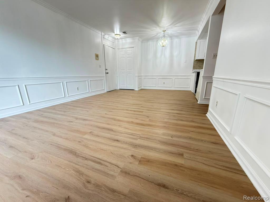 Spacious interior featuring wide plank wood-finish flooring, white paneled wainscoting, crown molding, and a decorative ceiling light fixture