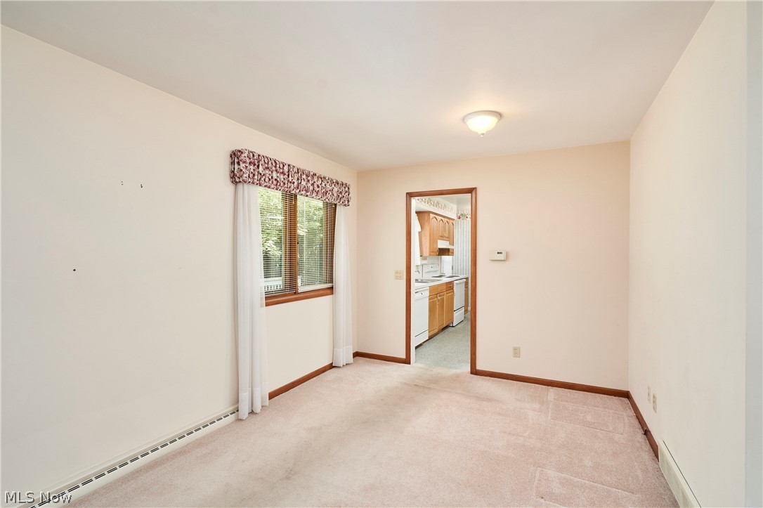 299 West Caston Road New Franklin, OH 44319 - Photo 17 of 23 Carpeted room with a window, baseboard heating, ceiling-mounted light fixture, and a doorway revealing a kitchen with wood cabinetry and white appliances