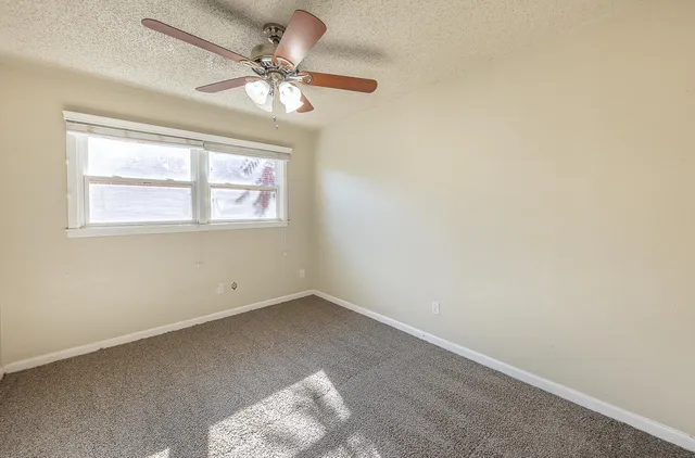 an empty room with a chandelier fan and windows