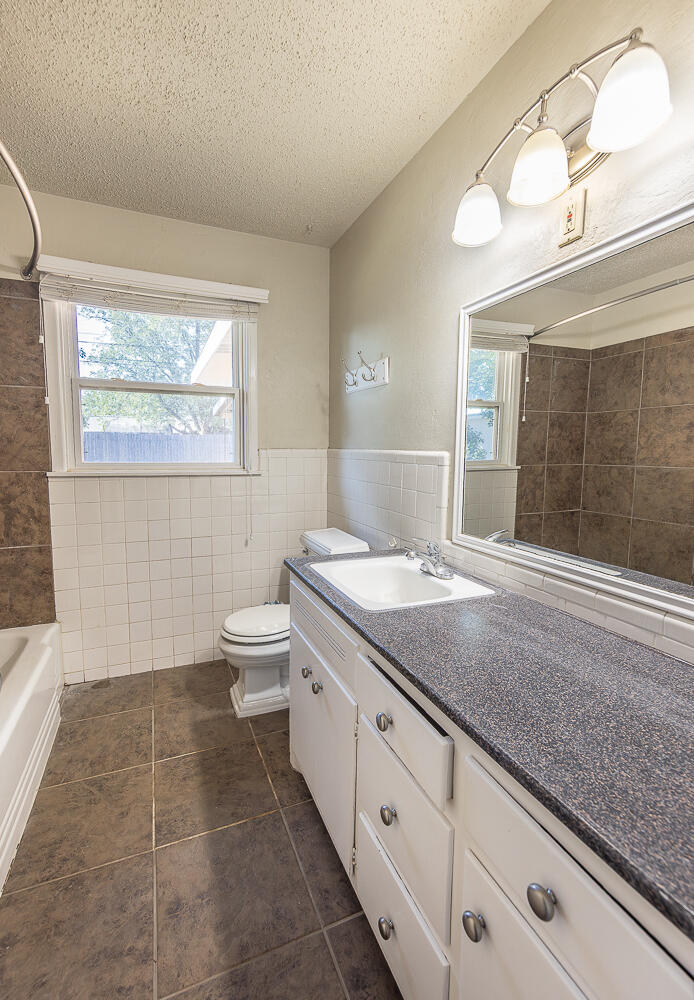 5017 46th Street Lubbock, TX 79414 - Photo 10 of 24 a bathroom with a granite countertop sink a toilet a mirror and shower