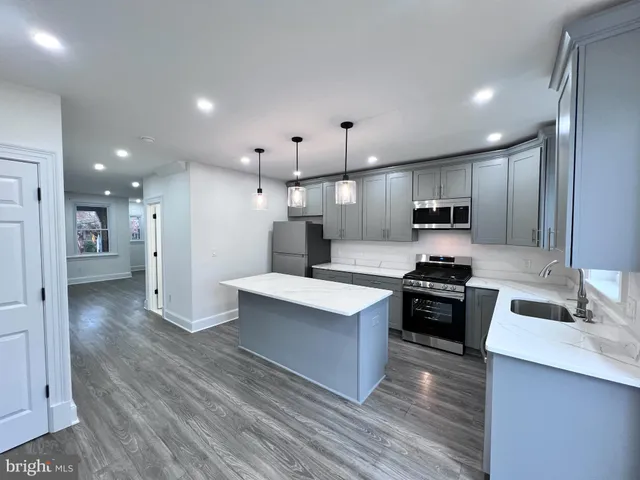 a kitchen with stainless steel appliances kitchen island a stove a sink a refrigerator and white cabinets with wooden floor