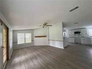 an empty room with wooden floor kitchen view and windows