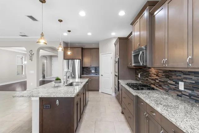 a large kitchen with granite countertop a large counter top a sink stainless steel appliances and cabinets