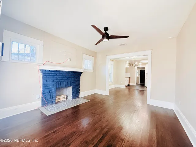 a view of an empty room with wooden floor fireplace and a window