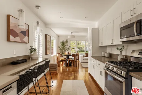 a kitchen with stainless steel appliances kitchen island granite countertop a stove top oven a sink a dining table and chairs with wooden floor