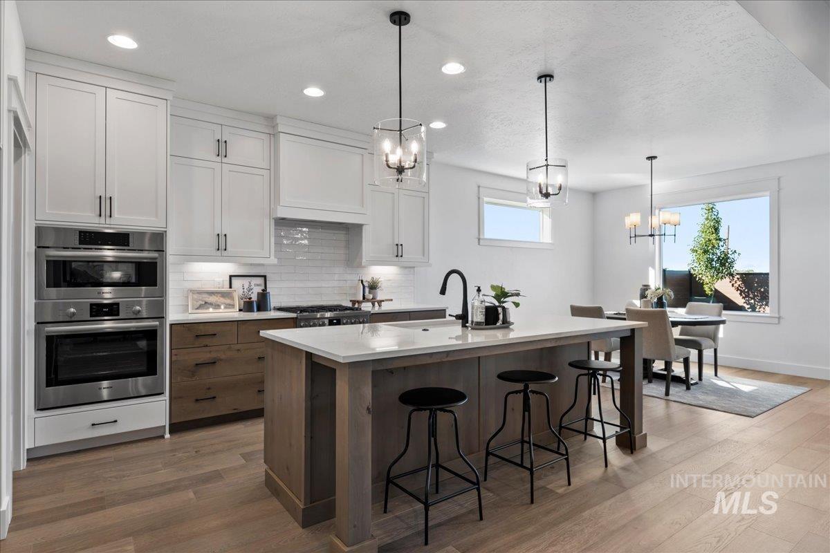 8150 West Gallup Street Meridian, ID 83646 - Photo 5 of 30 Kitchen with white cabinetry, decorative backsplash, decorative light fixtures, a breakfast bar area, and dark wood-type flooring