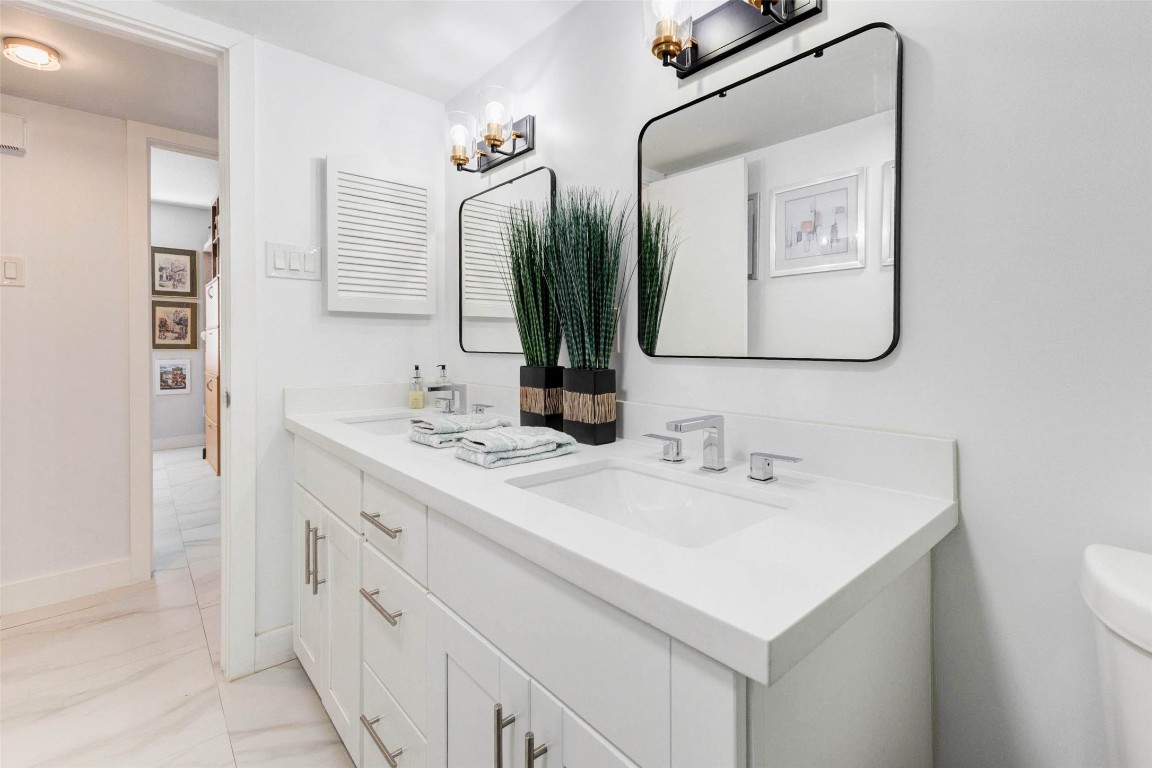 2234 South Piney Point Road, Unit 110 Houston, TX 77063 - Photo 16 of 25 Modern bathroom with a sleek double vanity, white cabinetry, and stylish square mirrors. The space is brightened by elegant light fixtures, and decorative plants add a touch of greenery.